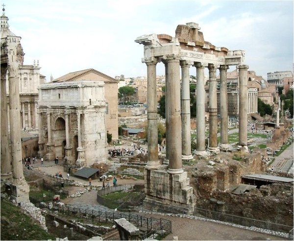 A color photograph shows a row of tall, weathered stone columns and other ruins with small groups of people walking at ground level.
