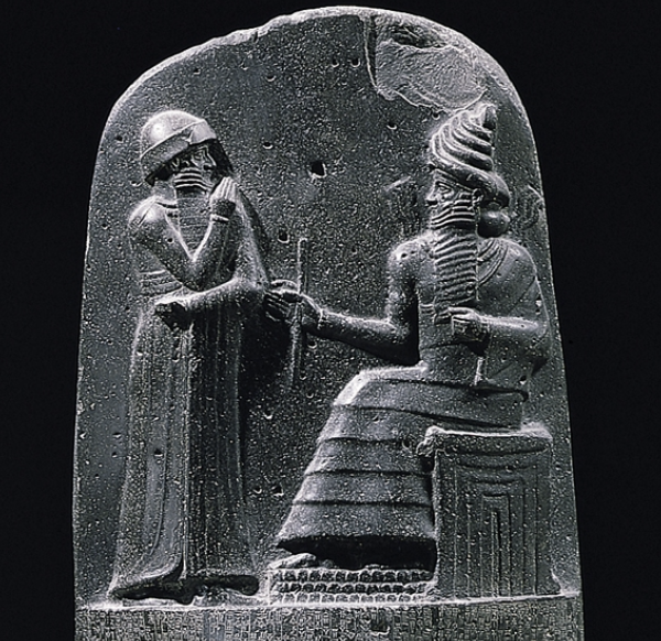 A dark, polished stone relief carving shows two human figures facing each other against a smooth, slightly curved stone surface. 