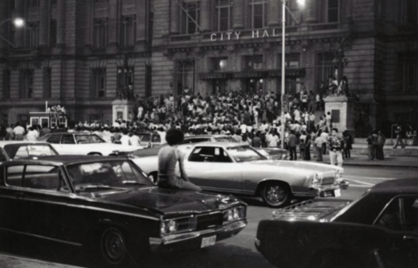 Black-and-white photograph captures a crowded street outside City Hall during a public gathering.