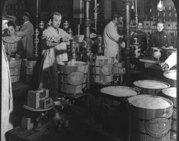 Black and white photo of workers in a meatpacking plant filling large buckets with lard. 